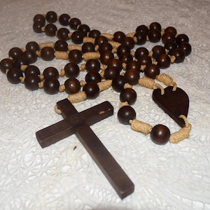 May include: A dark brown wooden rosary with large, round beads and a wooden cross. The beads are connected by a beige rope. The rosary also features a heart-shaped wooden piece.