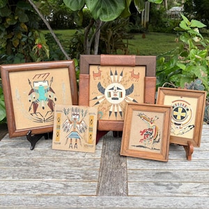 May include: A collection of five framed sand paintings featuring intricate geometric and figurative designs in earth tones, including depictions of stylized figures, animals, and circular motifs on a light tan background with wooden frames.