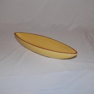 May include: A yellow, oblong-shaped dish with a brown trim. The dish has a smooth, glossy finish and is set against a white background. The design is simple and elegant, suitable for serving snacks or displaying small items.