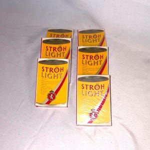 May include: Six vintage Stroh Light beer cans. The cans are yellow with red and white diagonal stripes and the words "STROH LIGHT" in red. The cans have a gold top and a crest logo.
