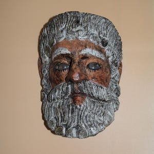 May include: A carved wooden mask with a white beard and a brown face. The mask has a detailed design and is a unique piece of art.