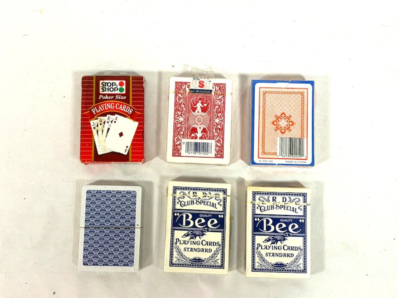 Puede incluir: Vista cenital de seis barajas de cartas. Las barajas son de varios colores y dise&ntilde;os, incluyendo rojo, azul y blanco. Algunas barajas est&aacute;n etiquetadas como "Stop Shop" y "Bee".