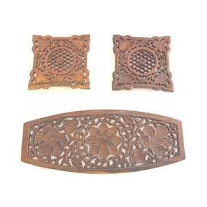May include: Three intricately carved wooden panels. Two square panels feature a central circular design surrounded by floral patterns. The third panel is a long, curved rectangle with a floral and leaf design. All panels are a warm brown color.