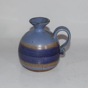 May include: A blue and brown ceramic pitcher with a rounded body and a handle. The pitcher has a light blue glaze with brown stripes.