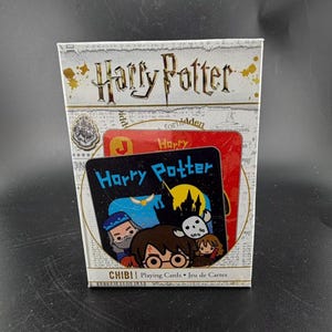 May include: A boxed set of Harry Potter Chibi playing cards. The box is white with gold lettering and a Harry Potter logo. The card design features cartoon illustrations of characters, with the words "Harry Potter" and "CHIBI" visible.