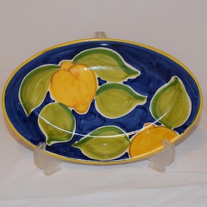 May include: An oval ceramic serving dish with a blue background and a yellow rim. The dish is decorated with green leaves and yellow lemons.