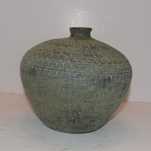 May include: A green ceramic vase with a textured surface and intricate geometric patterns. The vase has a rounded body and a narrow neck.