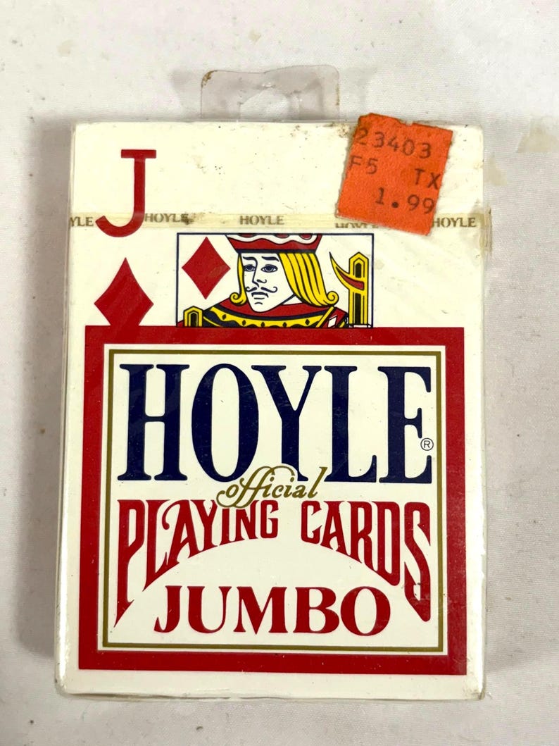 Puede incluir: Una baraja de cartas Hoyle Official, tama&ntilde;o Jumbo, en una caja blanca y roja. La caja presenta una ilustraci&oacute;n de la jota de diamantes y el logotipo de Hoyle en azul y rojo. Una etiqueta de precio naranja est&aacute; adjunta.