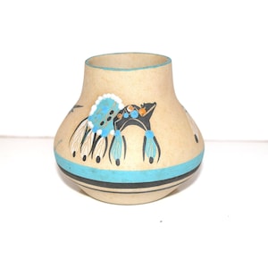 May include: A beige ceramic vase with a rounded body and a narrow opening. The vase features a turquoise band around the base and a decorative design of feathers and geometric shapes in black, turquoise, and orange.