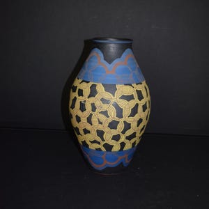 May include: A ceramic vase with a black, blue, yellow, and orange geometric pattern. The vase is oval shaped and has a wide mouth.