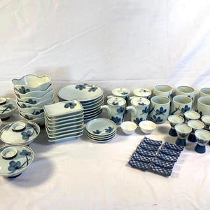 May include: A collection of white ceramic tableware with blue floral designs. The set includes bowls, plates, cups, saucers, and serving dishes. The tableware is arranged on a white surface, ideal for a dining setting.