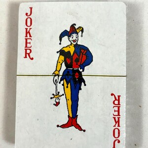 Puede incluir: Un mazo de cartas con una carta de Joker. La carta muestra un buf&oacute;n colorido con un atuendo rojo, amarillo, azul y negro. La palabra "JOKER" est&aacute; impresa verticalmente en rojo en ambos lados de la carta.