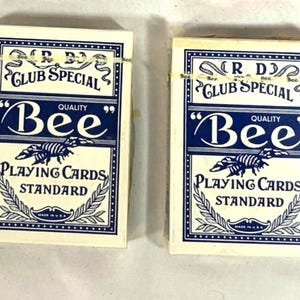 Puede incluir: Dos barajas de cartas "Bee". Las cajas de cartas son blancas con un dise&ntilde;o azul marino. El texto en la caja dice "R.D. Club Special", "Bee Quality" y "Playing Cards Standard". Las cajas est&aacute;n sujetas con una goma el&aacute;stica.