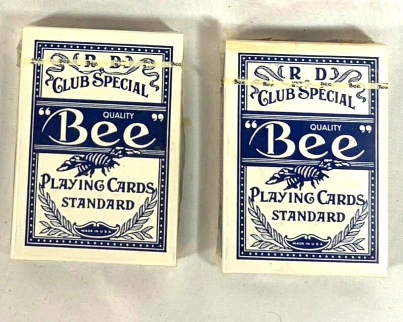Puede incluir: Dos barajas de cartas "Bee". Las cajas de cartas son blancas con un dise&ntilde;o azul marino. El texto en la caja dice "R.D. Club Special", "Bee Quality" y "Playing Cards Standard". Las cajas est&aacute;n sujetas con una goma el&aacute;stica.