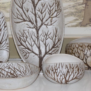 May include: Set of four white ceramic bowls with a brown tree branch design. The bowls are in various shapes and sizes.