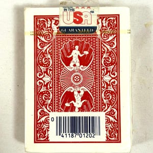 Puede incluir: Una baraja de cartas sellada con un dise&ntilde;o rojo y blanco. El reverso de la carta presenta un patr&oacute;n sim&eacute;trico con una figura central y detalles ornamentados. El embalaje incluye el texto "MADE IN THE USA" y un c&oacute;digo de barras.