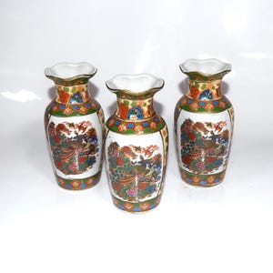 May include: Three decorative ceramic vases with a white base, featuring a colorful peacock design. The vases have a ruffled rim and are adorned with orange, green, and blue floral patterns. The vases are approximately 6 inches tall.