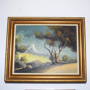 Op de afbeelding: Olieverfschilderij van een landschap in een gouden lijst. Het kunstwerk toont een boom met donkergroene en bruine bladeren, een berg en een bewolkte lucht. Het schilderij heeft een textuur.