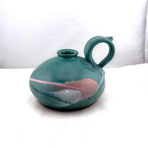 May include: Teal ceramic pitcher with a rounded body and a loop handle. The pitcher features a pink and white abstract design. The spout is small and the opening is circular. The pitcher is a decorative item.