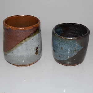 May include: Two ceramic cups, one with a brown, white, and blue glaze, and the other with a brown, white, and blue glaze.
