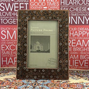 May include: A rectangular tabletop picture frame with a dark brown, textured border featuring intricate floral-shaped cutouts and small white bead accents. The frame holds a display card labeled Tabletop Picture Frame 4 in x 6 in, Made in India.