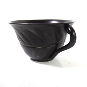 May include: A white ceramic mug with a black handle and the text "But First, Coffee" in a black, bold font. The mug is sitting on a wooden surface. The mug is 4 inches tall.