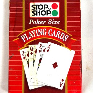 Puede incluir: Una baraja de cartas de p&oacute;quer de la marca "Stop & Shop". La caja roja y blanca presenta el logotipo de Stop & Shop y las palabras "Poker Size" y "Playing Cards". Las cartas est&aacute;n abanicadas, mostrando el As de diamantes y otras figuras.