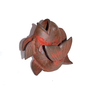 May include: A brown fish sculpture with red accents. The fish has an open mouth and detailed fins and tail. The sculpture is made of a textured material and is set against a white background.