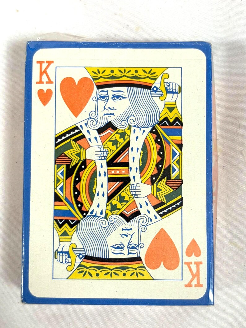 Puede incluir: Una baraja de cartas con el Rey de Corazones. El dise&ntilde;o de la carta incluye una corona amarilla, una ilustraci&oacute;n detallada de un rey y el s&iacute;mbolo del coraz&oacute;n. La baraja tiene un borde azul.