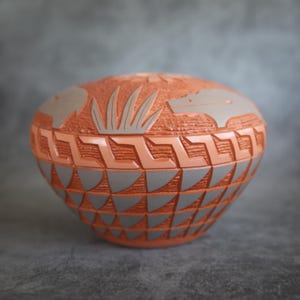 May include: A hand-carved terracotta pottery bowl with a geometric design and a depiction of animals and plants. The bowl is a light orange color with gray accents.