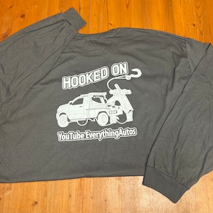 May include: Dark gray long-sleeve shirt with a white graphic of a tow truck and the words "HOOKED ON" above it. Below the truck is the text "YouTube EverythingAutos". The shirt is made of a soft material.