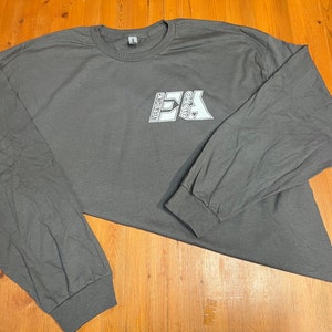 May include: A charcoal gray long-sleeve t-shirt with the text "EVERYTHING AUTO" in a white, blocky font. The shirt has a crew neck and ribbed cuffs. The shirt is made of a soft material.