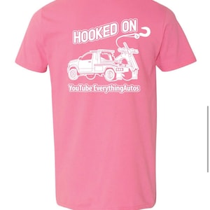 May include: Pink t-shirt with a white graphic of a tow truck and the words "HOOKED ON" and "YouTube EverythingAutos". The design is centered on the back of the shirt.
