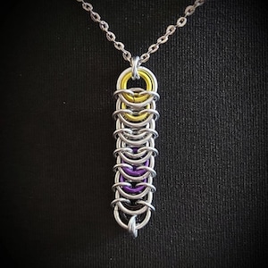 May include: A silver chain necklace with a pendant made of interlocking metal rings. The rings are silver, purple, and yellow, creating a layered effect.