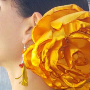 May include: A large, bright yellow flower made of satin fabric. The flower is worn as a hair accessory.