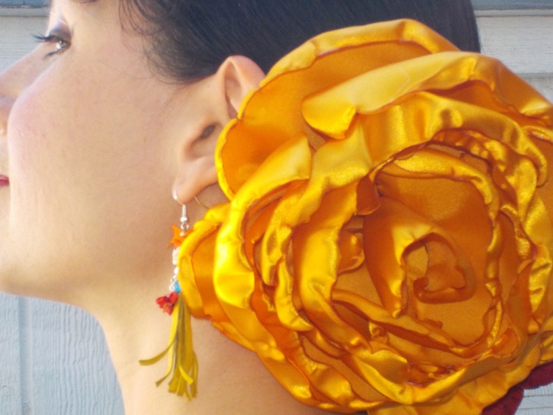 May include: A large, bright yellow flower made of satin fabric. The flower is worn as a hair accessory.
