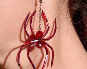 Puede incluir: Pendiente de araña roja con diseño de cuentas. La araña tiene un cuerpo redondo y patas largas, conectada a un gancho para la oreja por una cadena. Una pieza de joyería única.