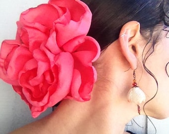 May include: A large, bright pink fabric flower hair clip. The flower is made of several layers of fabric petals and is worn in the hair of a person with dark hair.