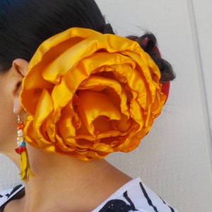 May include: A large, bright yellow satin flower hair clip. The flower is made of multiple layers of fabric and has a ruffled texture.