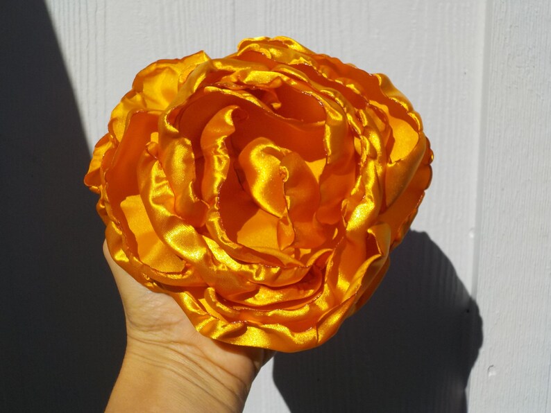 May include: A large, bright yellow satin flower with multiple layers of petals.