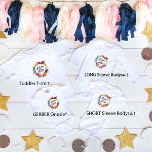 Op de afbeelding: Drie witte shirts met de tekst "stylish littles" in een krans van bloemen. De shirts zijn een T-shirt voor peuters, een romper met lange mouwen en een romper met korte mouwen.
