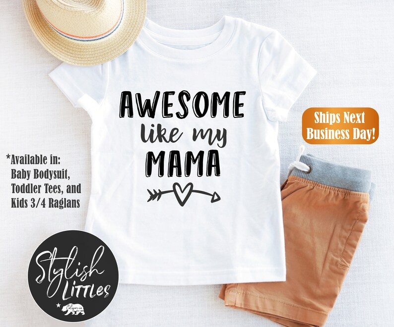 Op de afbeelding: Wit T-shirt met zwarte tekst die "AWESOME like my MAMA" luidt, met een pijl- en hartvormig motief. *Beschikbaar in: Baby-romper, peuter-T-shirts en kinder-3/4-raglans. Stylish LITTLES.