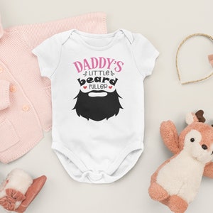 May include: White baby onesie with short sleeves and the text "Daddy's Little beard puller" in pink with a black beard graphic.