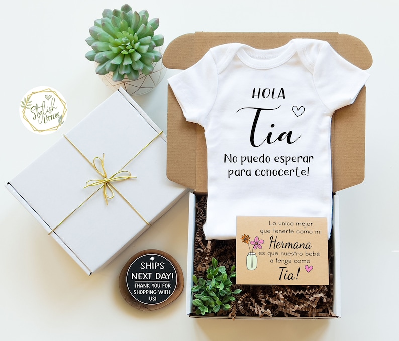 May include: A white baby onesie with the text "HOLA Tia No puedo esperar para conocertel!" in black. A brown card with the text "Lo unico mejor que tenerte como mi Hermana es que nuestro bebe a tenga como Tia!" in black and pink. The card has a small illustration of a mason jar with flowers.