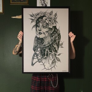 May include: A black and white drawing of a woman with a floral crown and a skeletal ribcage. The woman's face is partially obscured by the flowers. The drawing is framed in a black frame.