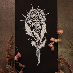 May include: A black rectangular patch featuring a white floral design with thorns and leaves. The detailed illustration has a gothic or vintage aesthetic. The patch is likely made of fabric and is suitable for sewing or ironing onto clothing or accessories.