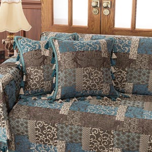 May include: A patchwork sofa throw with a blue and brown color scheme. The throw features a variety of patterns and textures, including paisley, floral, and geometric designs. The throw is accented with tassels along the edges.
