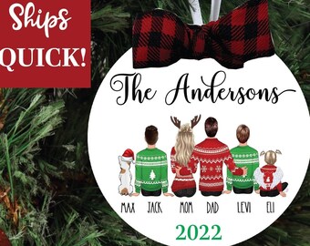 May include: White round Christmas ornament with a red and black plaid bow. The ornament features a family of six in matching Christmas sweaters, a dog, and the text "The Andersons 2022".