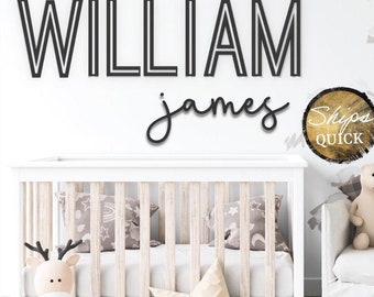 May include: Black wooden name sign spelling "WILLIAM james" above a white crib. The word "WILLIAM" is in a bold, block font, while "james" is in a cursive script. A stuffed deer, star, and bear are in the nursery.