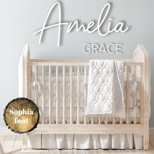 May include: A white wooden crib with a white quilted blanket and a white ruffle skirt. The crib is decorated with a white sign that says "Amelia Grace" in a cursive font.